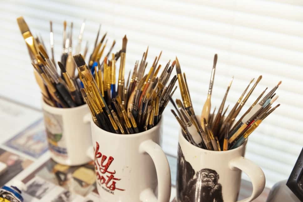 Coffee mugs filled with paintbrushes in Zeek’s home studio.