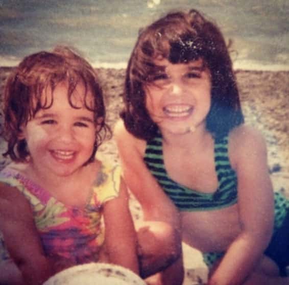 Alysse and her sister, as children, smile at the camera during a beach vacation.