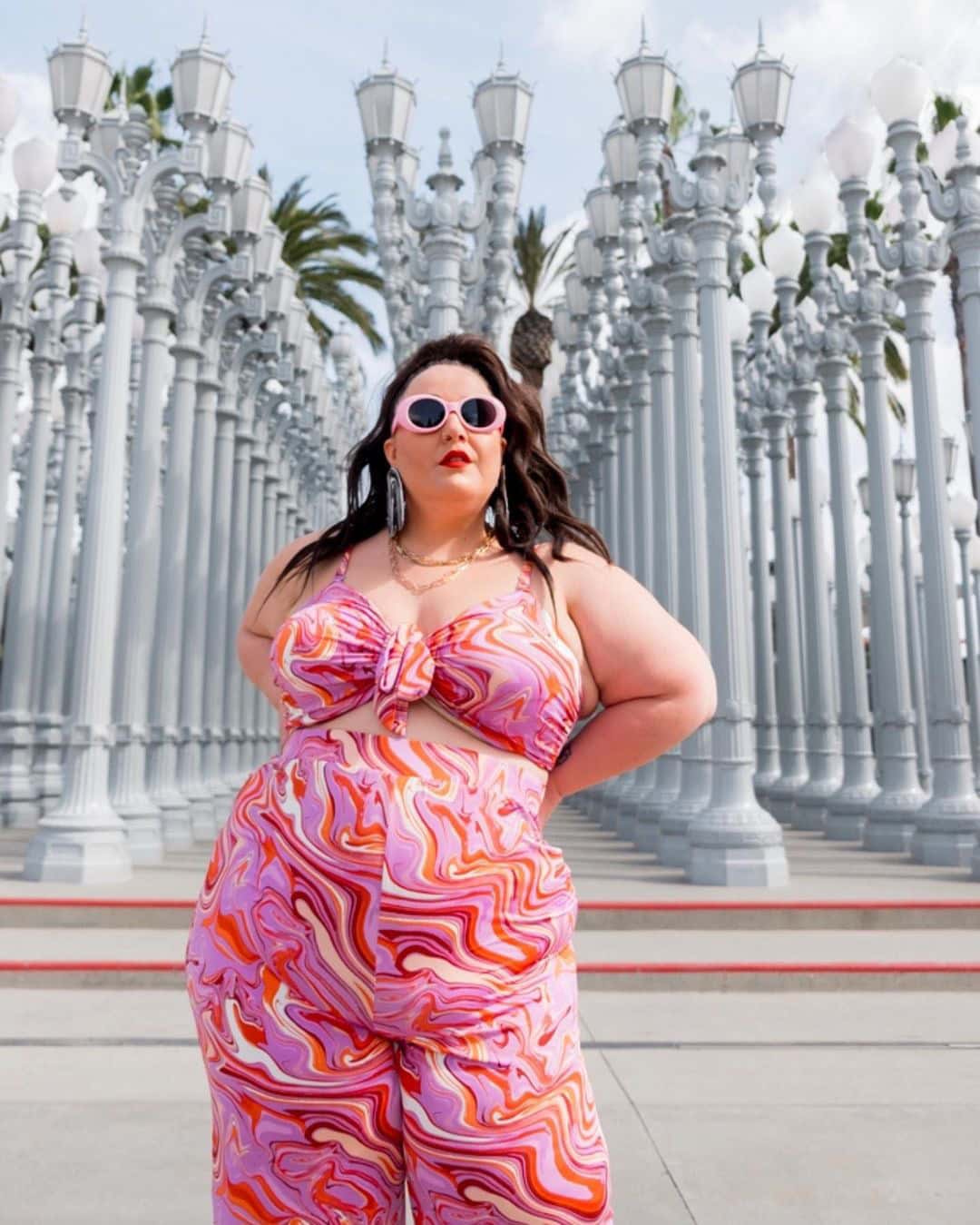 Alysse strikes a pose in a flamboyant pink outfit and pink-framed sunglasses.