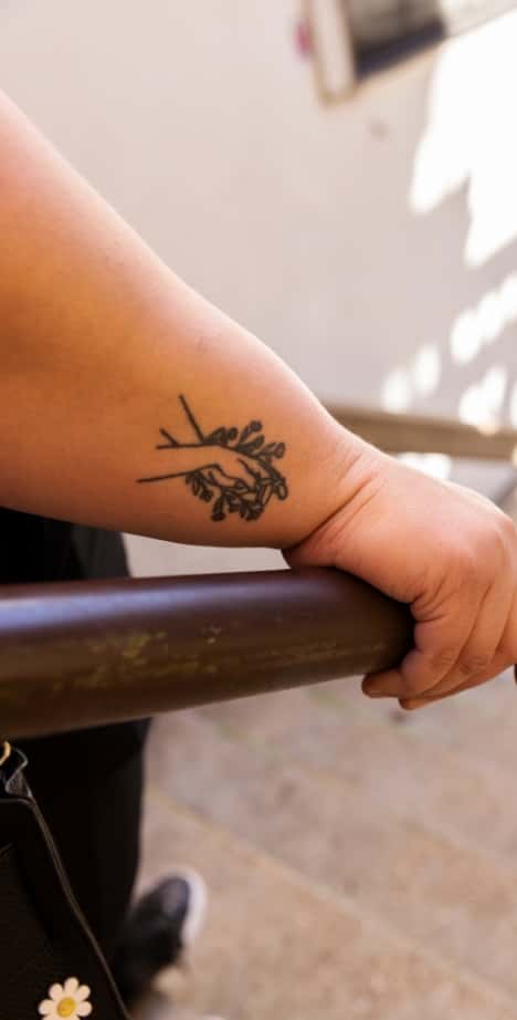 A close-up of a tattoo on Alysse’s wrist, which shows hands intertwined with flowers.