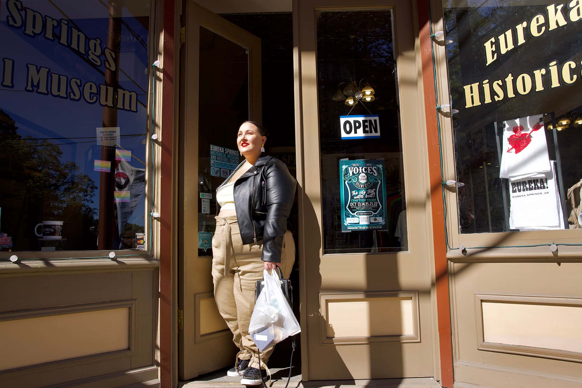 Alysse in front of the Eureka Springs Historical Museum, with rainbow flag stickers visible in the window.