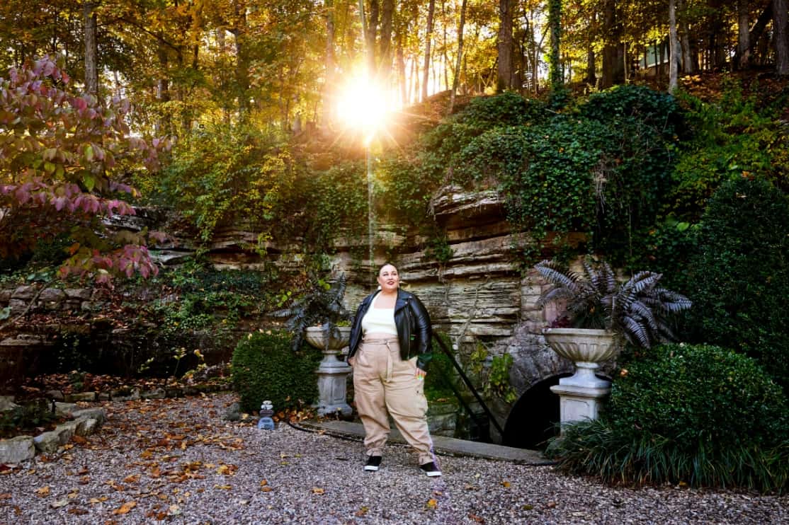 Alysse, wearing a leather biker jacket and casual khaki cargo pants, surrounded by Eureka Springs’ tumbling greenery.