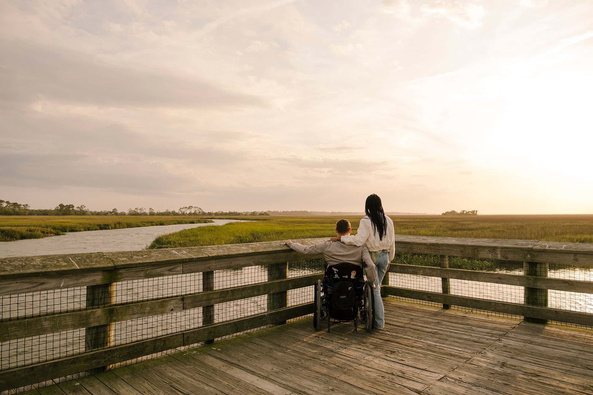 Cole and Charisma look out at the salt marshes on the Marsh Boardwalk Trail at sunset.