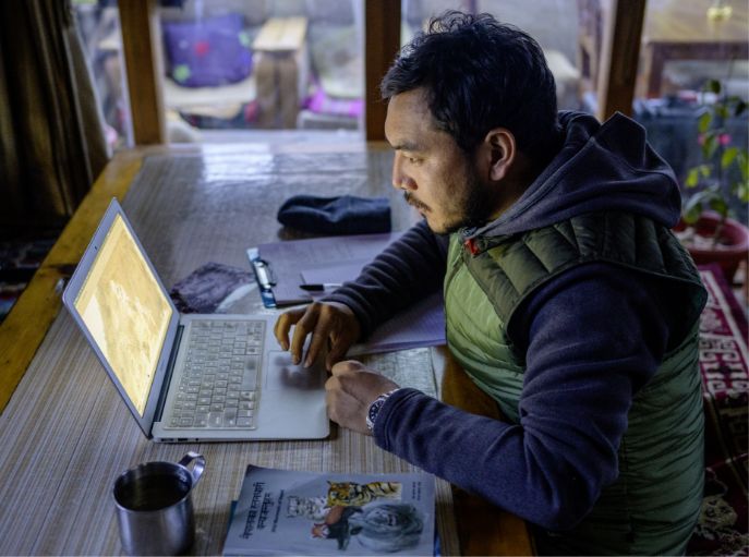Rinzin Phunjok Lama at his laptop, editing photos of wildlife captured by camera traps.