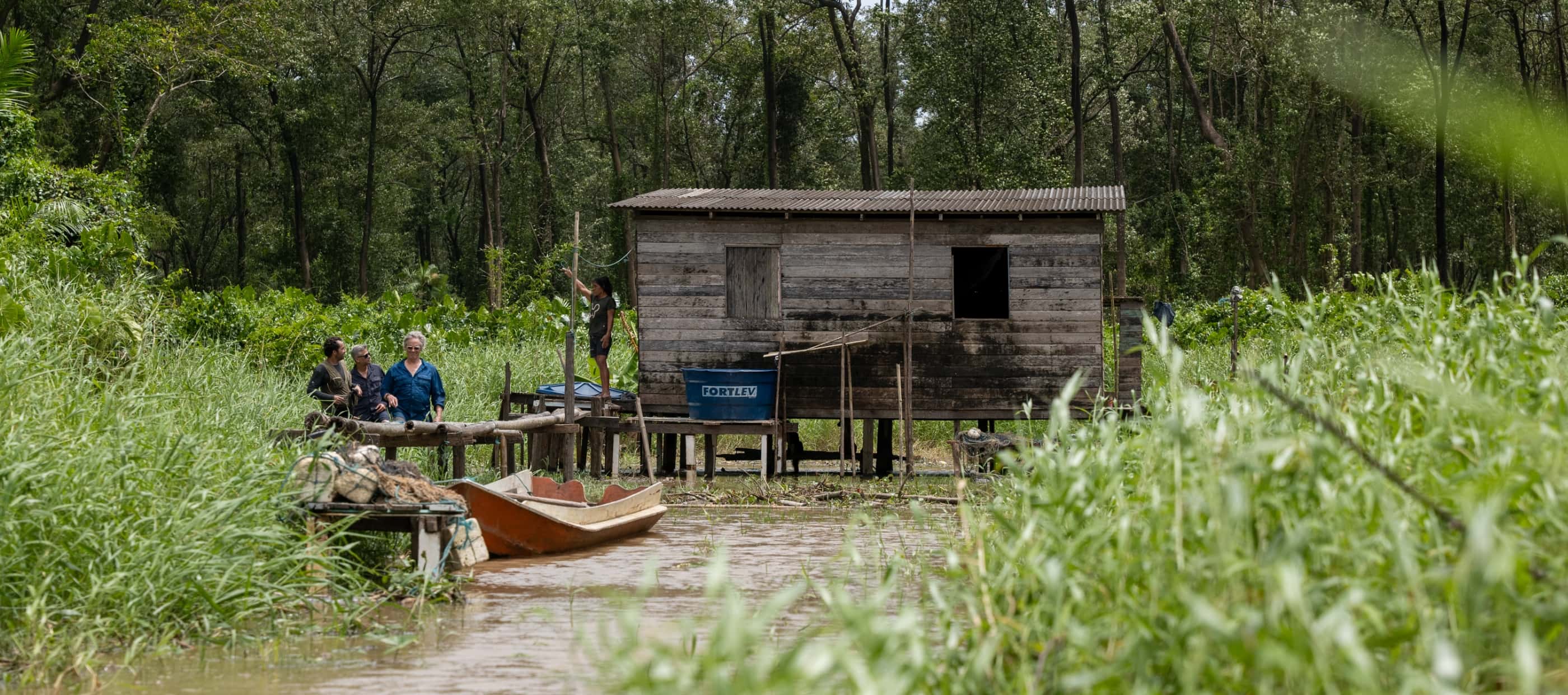 National Geographic Explorers Angelo Bernardino and Margaret Owuor interview locals outside a wooden stilt house in an Amazon coast community.