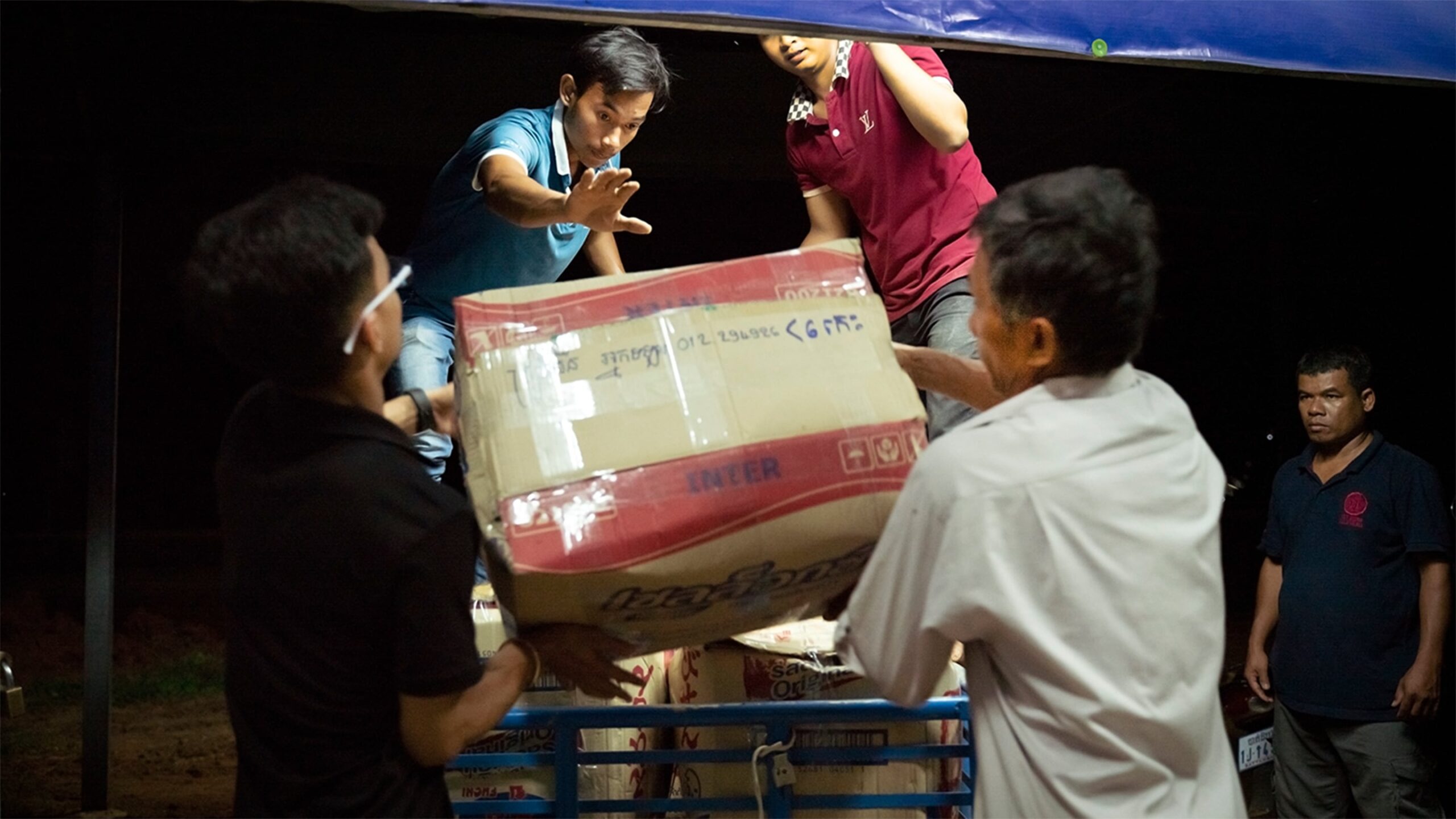 Lach Song, center left, guides a box of freshly packed vegetables onto a cart to wait for a late-night bus pickup that will deliver the farmers' vegetables from this packinghouse near Battambang to markets in Phnom Penh. Photo credit: Max Fannin for UC Davis 