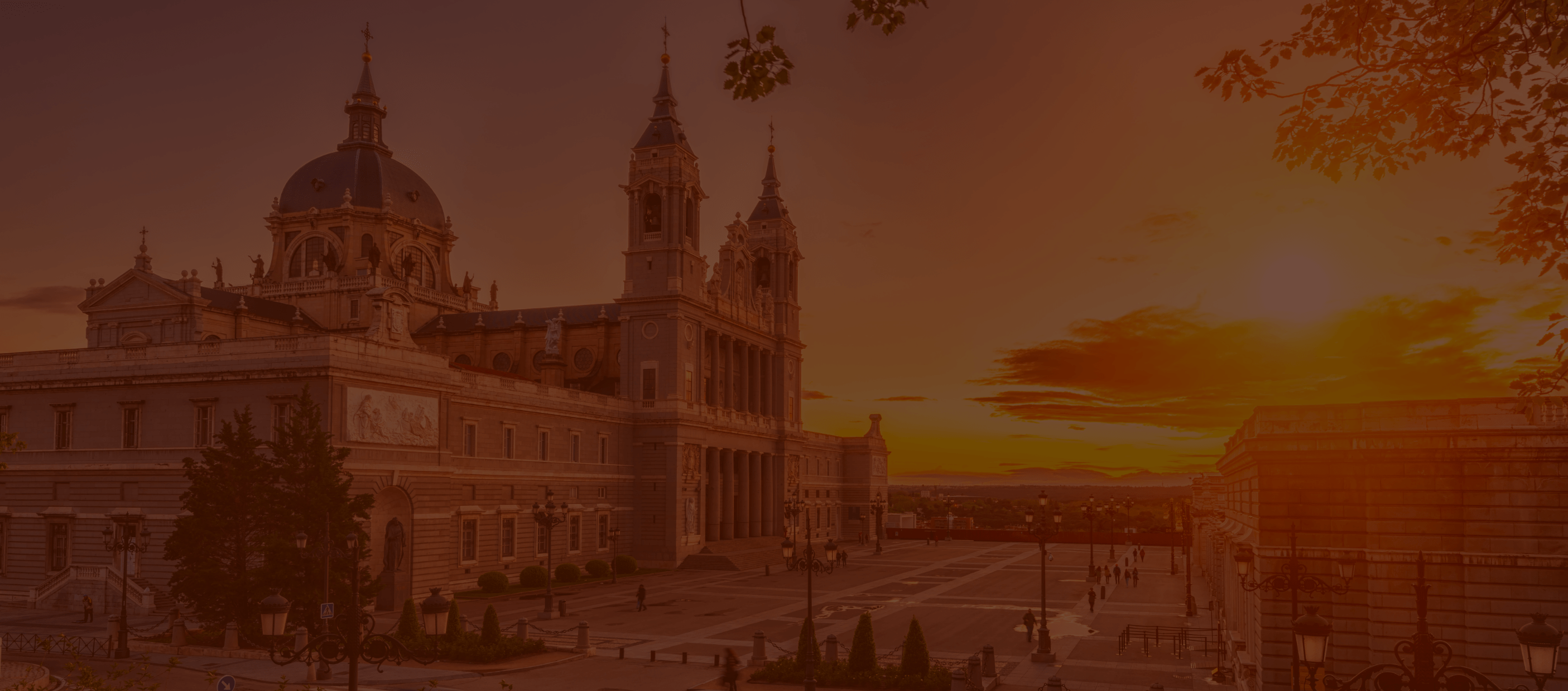 A sunset casts a warm orange glow over the grand La Almudena cathedral in Madrid.