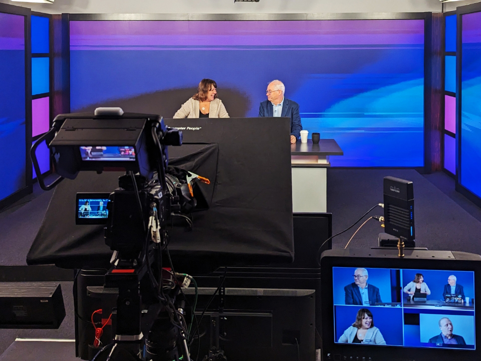 A television studio with two people in front of a camera.