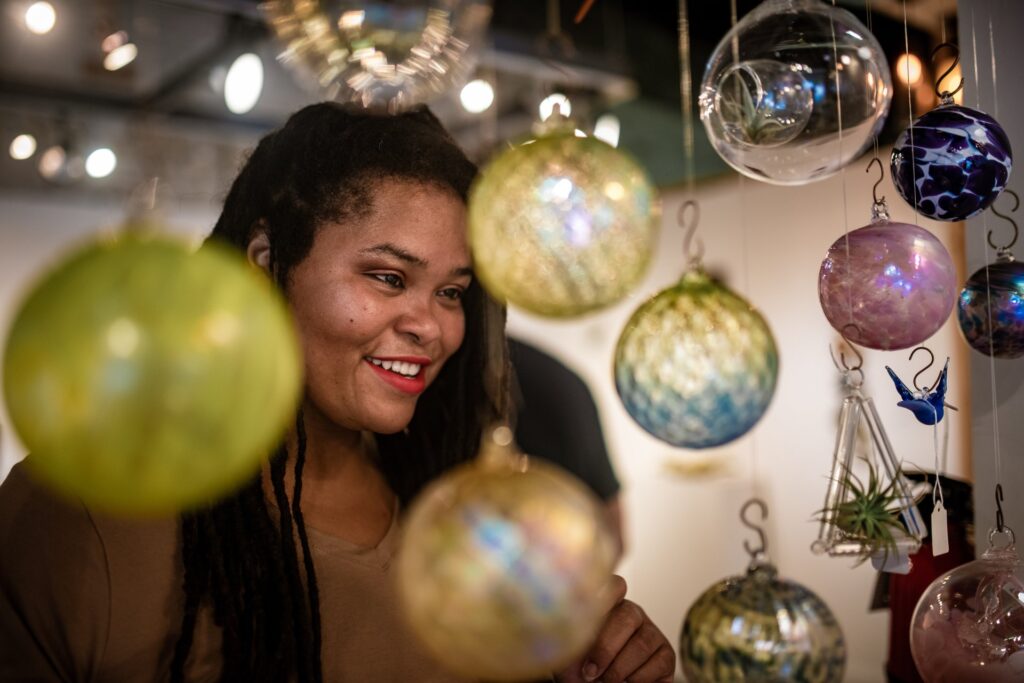 A woman smiles while looking at glass ornaments.