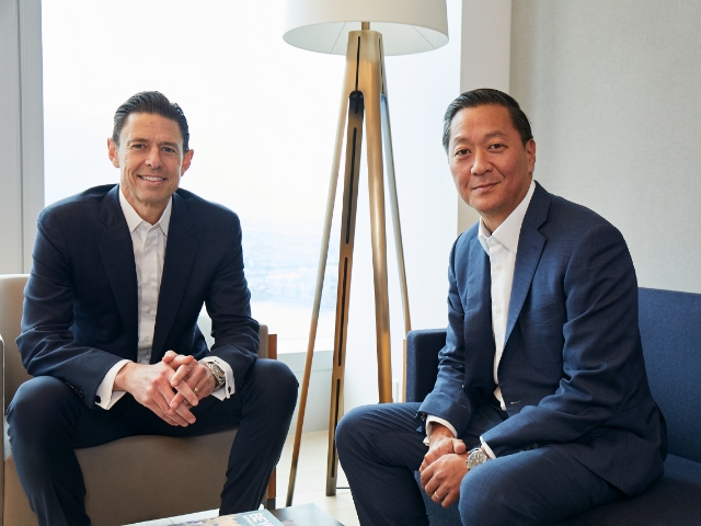 Two men in business suits sitting on a couch.
