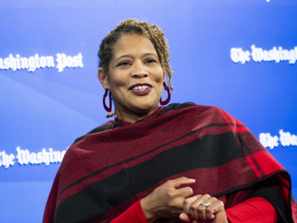 A woman in a red scarf standing in front of a blue background.