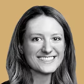A smiling person with long hair is seen against a solid beige background.