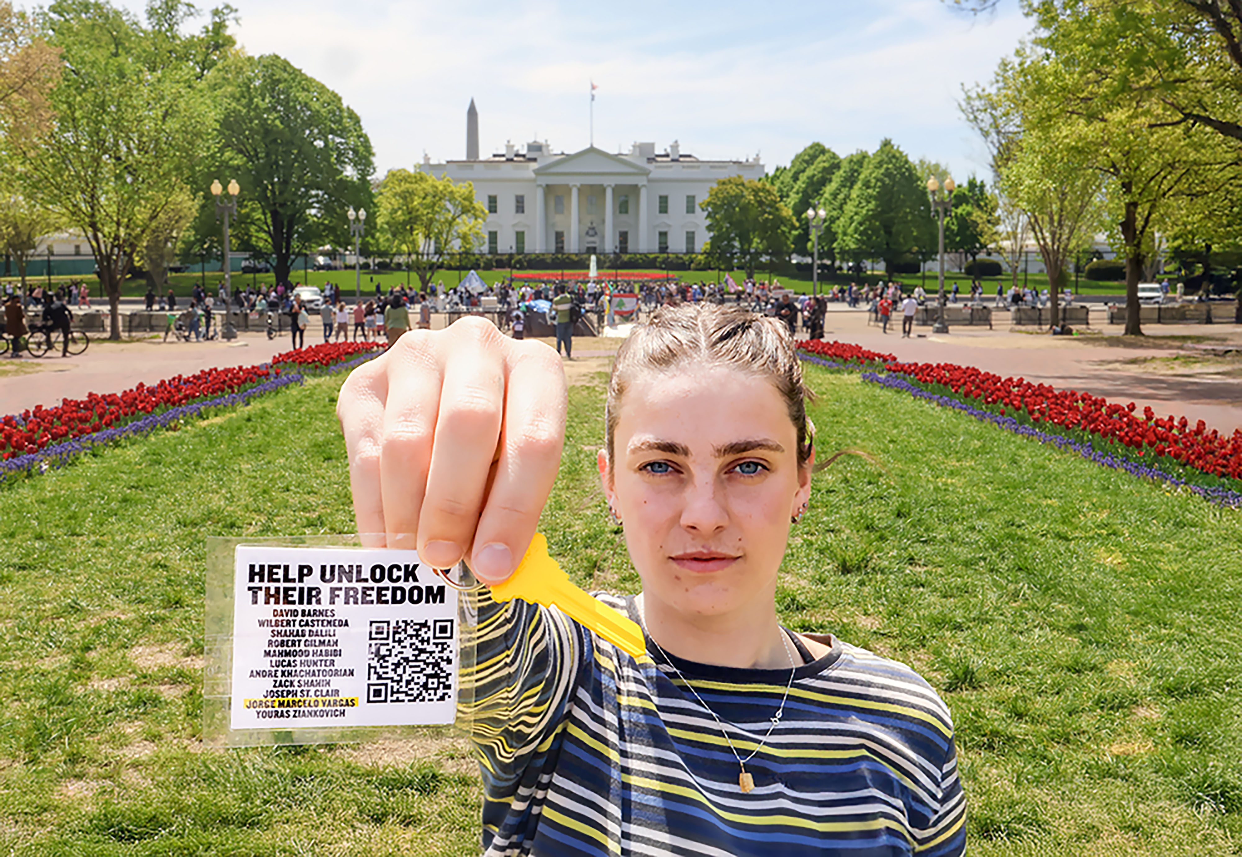A person stands in front of the White House holding a flyer that reads, "Help Unlock Their Freedom" with a QR code and additional text.