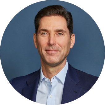 A man with short dark hair wearing a blue suit jacket and light blue shirt poses in front of a plain blue background.