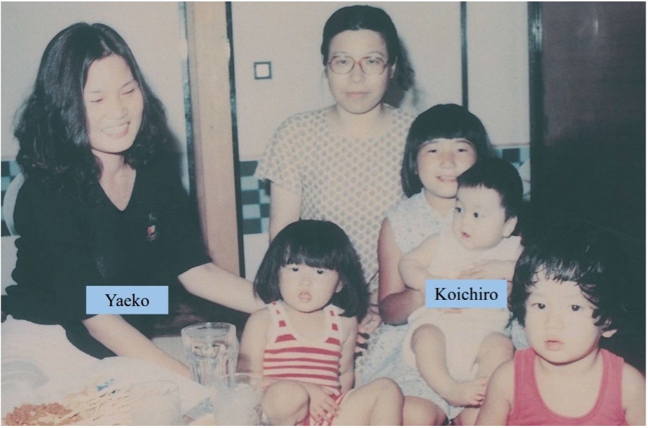 A family photo of six people indoors; two adults and four children, with "Yaeko" and "Koichiro" labeled on a woman and a baby, respectively.