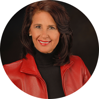 Woman with shoulder-length dark hair wearing a red leather jacket over a black turtleneck, smiling at the camera against a dark background.