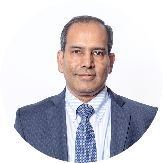 A man in a navy blue suit, light blue shirt, and patterned tie poses for a professional headshot against a plain white background.