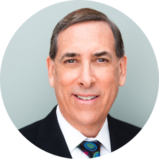 Man in a suit and tie smiling at the camera with a light gray background.