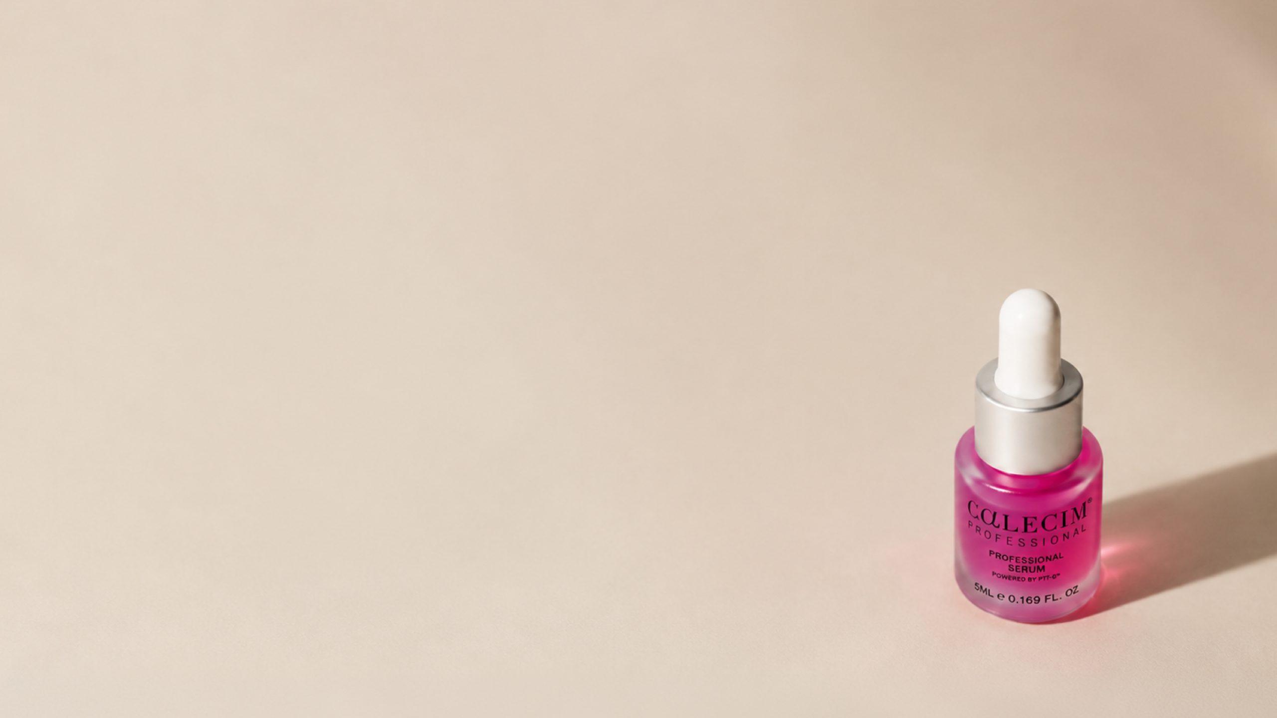 Small pink serum bottle with a white dropper cap is placed on a light beige surface, positioned in the lower right corner of the image.